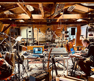 Muzikanten van Veenfabriek werken tussen instrumenten en geluidsapparatuur in de monumentale zolder van Scheltema in Leiden. Foto: Yonga Sun